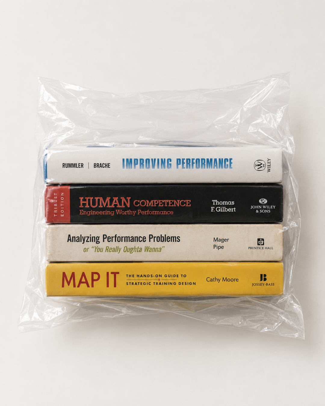 Four performance-improvement books — Improving Performance, Human Competence, Analyzing Performance Problems and Map It — stacked and sealed inside a clear plastic bag.