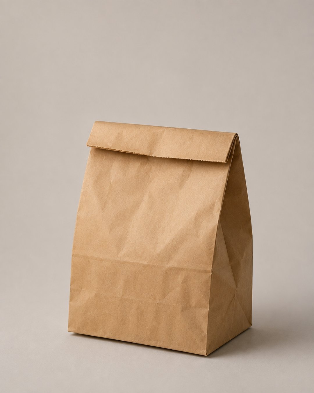 A plain brown paper bag, folded shut at the top, standing on a light grey surface.